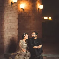 An intimate moment during a Sangeet night. The couple shares a quiet conversation under the warm glow of wall lights, a peaceful pause in the middle of the celebration.