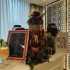 A stylishly decorated bar corner for a proposal or anniversary celebration. The setup includes deep red roses, copper barware, a framed menu, and a playful sign that reads "You are the GIN to my TONIC."