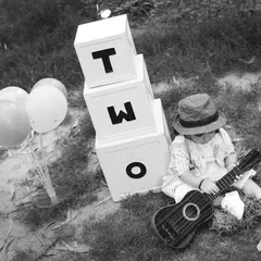 A black and white photo of a two-year-old boy playing a small guitar during his outdoor session. We encourage play to bring out natural expressions.