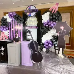 A side angle of the 'Wednesday' birthday party decor, highlighting the depth and various elements of the setup. This view shows the cello prop, character cutouts, and layered balloon arrangements that bring the theme to life.
