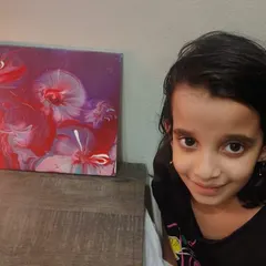 A young creator proudly posing next to her finished floral-like abstract painting. The patterns and colors in acrylic pouring are always a beautiful surprise.