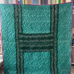 This reversible memory quilt showcases the beauty of a teal green saree. The original borders are used to create a striking 'H' pattern, and the entire piece is finished with a swirling rose stitch.