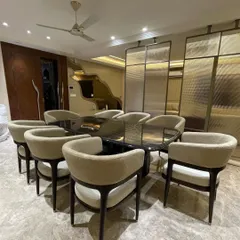 An angled view of the 8-seater luxury dining set, showing the high-gloss finish on the table legs and the beautiful black stone top. The chairs are arranged to showcase their elegant, curved form.