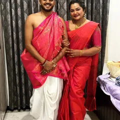 A beautiful moment from a client's special day. She is wearing our elegant red saree, and he is in a traditional silk dhoti and angavastram, showing how we cater to the whole family.