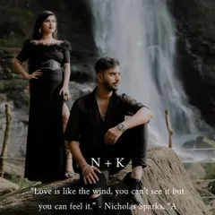 A dramatic and stylish portrait from an outdoor couple's photoshoot. The couple is posed on a rock with a stunning waterfall behind them, creating a cinematic and memorable image that speaks to their adventurous spirit.