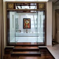 A modern and minimalist approach to a pooja room, designed with clear glass walls to maintain an open feel. The space is defined by a dark wood frame and elevated wooden steps, leading to a simple white platform for prayer.