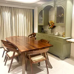 The dining area is anchored by a custom live-edge wooden table, providing an organic contrast to the sophisticated, muted green crockery unit. This space was designed for both family meals and elegant entertaining, balancing functionality with refined aesthetics.
