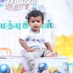 A portrait of baby Matthew at his birthday celebration. Seated in front of a colorful balloon backdrop with his name in Tamil, this shot captures the festive atmosphere of the event.
