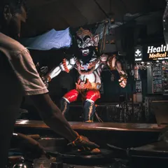 A street food vendor works at his stall, with the imposing figure of a Narakasura effigy looming in the background.