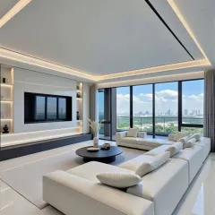 A bright and airy living room with panoramic city views through floor-to-ceiling windows. We used a long, white sectional sofa to maximize seating and maintain an open feel. The custom TV unit with integrated shelving and subtle backlighting provides a sleek focal point without overwhelming the space.