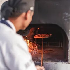 Our chef carefully rotates a pizza inside the wood-fired oven. This technique, known as "doming," ensures the toppings are perfectly cooked and the cheese is melted while the crust gets its final char.