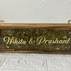 A beautiful wooden frame nameplate, filled with preserved green and yellow flowers. The couple's names in gold script stand out beautifully against the floral background.