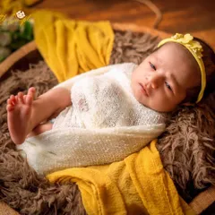 An alert and curious expression from a baby nestled in a wooden bowl. The contrast of the bright yellow headband and the rustic props makes this shot pop.