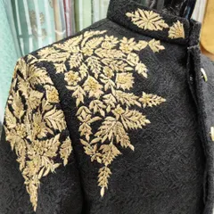A close-up of the gold hand embroidery on a black Jodhpuri suit. The leaf-patterned threadwork is meticulously crafted to create a rich and luxurious texture.