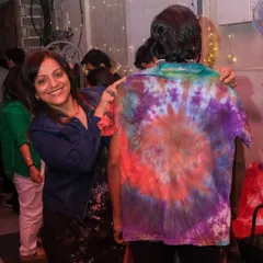 A smiling participant points to the back of a brightly colored tie-dye shirt, a fantastic result from one of our group craft events.