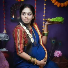 This portrait captures elements of a traditional Dohale Jevan or baby shower ceremony. The gajra in her hair, the plate of fruit, and the festive background celebrate this important milestone.