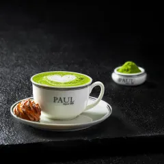 A hot matcha latte with delicate heart-shaped foam art, served in a classic Paul branded cup.