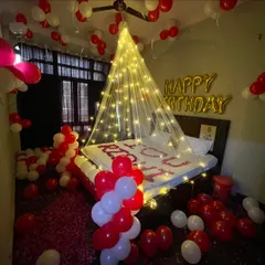 This is my classic romantic birthday decoration, perfect for surprising your partner. I use a canopy of fairy lights to create a dreamy focal point over the bed, complemented by hundreds of red and white balloons and rose petals on the bed and floor.