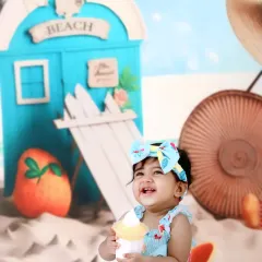 A baby girl laughs with delight while holding a toy ice cream cone during her fun-filled beach-themed photoshoot.