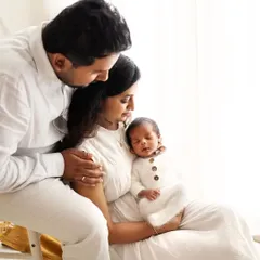 The new family of three, all dressed in white, admiring their little one. The soft, natural light creates a beautiful, airy feel.