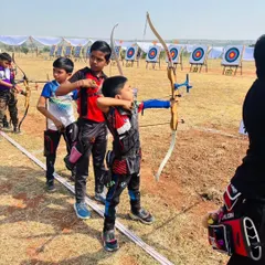 An older student helps a younger archer with his form, showcasing the supportive community we build among our students during a state competition.