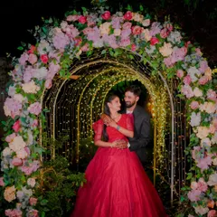 A romantic couple's portrait under a beautifully lit floral arch at night. This is a popular setup for pre-wedding photography, creating a magical and intimate atmosphere.