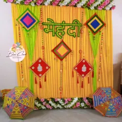A traditional Mehendi ceremony backdrop with yellow and green drapes, marigold flowers, and colorful Rajasthani umbrellas.