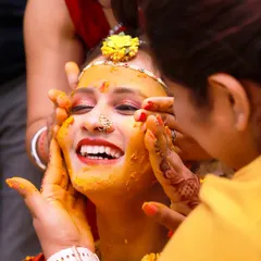 A candid shot capturing the pure joy of a bride during her Haldi ceremony, her face lit up with a wide smile as family applies turmeric paste. These unscripted moments of happiness are what make wedding photography so special.