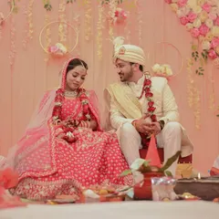 A candid moment during the wedding ceremony. The couple shares a look while seated at the mandap, surrounded by family and beautiful pastel floral decor.