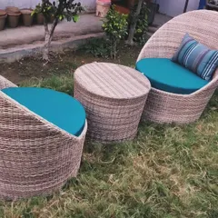 This two-seater coffee set features unique, deep-seated "cup" chairs made from woven wicker. Paired with a matching wicker table and vibrant teal cushions, this set is perfect for a small balcony or a cozy garden corner, offering a stylish and comfortable spot for two.