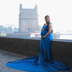 Another perspective of this incredible shoot, showing the beautiful mom-to-be posing by the water. The long train of the royal blue gown drapes elegantly, adding a touch of royalty to the cityscape.
