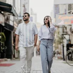 A candid shot of a couple strolling through a city lane, sunglasses on, looking effortlessly stylish. This captures the dynamic energy of a city-based pre-wedding photoshoot.