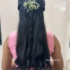 A beautiful and intricate half-up, half-down hairstyle for a guest. This style features a central braid accented with pearls and a spray of baby's breath for a delicate touch.