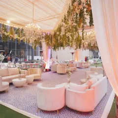 An elegant outdoor lounge setup for a reception, with plush white sofas, hanging florals, and beautiful chandeliers.
