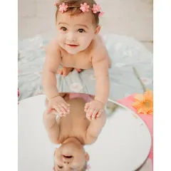 I love using creative props like this mirror to add a touch of magic to outdoor sessions. This baby girl, wearing a sweet floral headband, is fascinated by her own reflection, creating a unique and engaging portrait for her first birthday shoot.