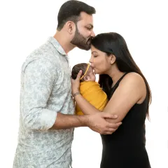 A beautiful first family photo. Both parents share a kiss over their newborn, creating a portrait that is overflowing with love and happiness.