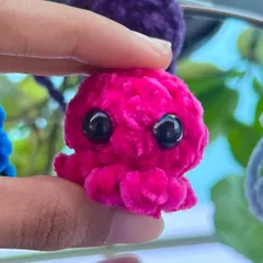 A close up of the mini octopus keychain in a vibrant hot pink. The soft, fluffy yarn and big eyes make it extra cute.