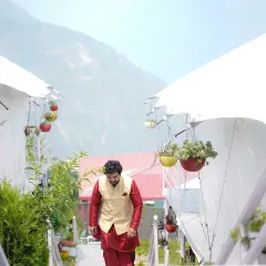 The groom's entrance. This shot captures him walking down a path lined with modern tents at a destination wedding, creating a sense of anticipation.