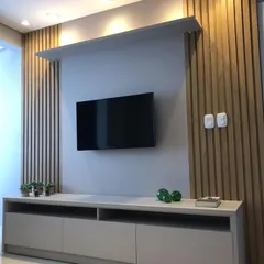 A sleek and modern TV unit design. This unit combines a simple grey console with natural wood-fluted paneling and an overhead shelf with spotlights, creating a stylish focal point for the living room.