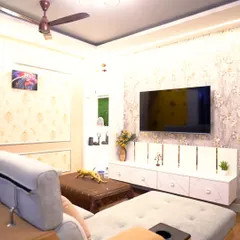 A cozy and luxurious living room featuring a comfortable L-shaped sofa, elegant wallpaper, and a modern TV unit. The false ceiling with dual-tone lighting adds warmth and sophistication to the space.