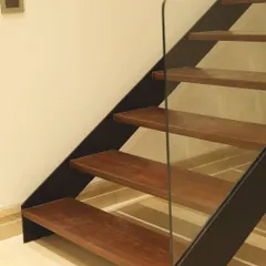 A close-up of the minimalist staircase in the "House of Frames," featuring warm wooden treads and a sleek glass balustrade. This detail exemplifies our commitment to clean lines and high-quality materials in every aspect of our interior architecture.
