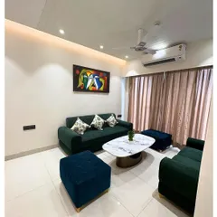 A cozy and contemporary living room setup in a 3BHK at ATS Advantage. The dark green sofa pairs beautifully with blue ottomans and a marble-top coffee table for a balanced, modern look.