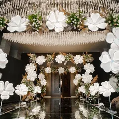 An enchanting entrance designed with oversized, illuminated white blossoms and pampas grass. The mirrored floor reflects the glowing flowers, creating a dreamlike and immersive welcome for guests.