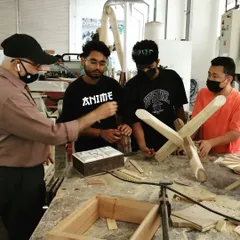 An instructor discusses different joinery techniques with students, using examples of a finished box and a cross-lap joint to illustrate his points.