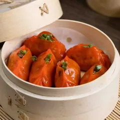 A steamer basket filled with our bright orange dim sum. Each dumpling is packed with a savory filling and garnished with fresh spring onions, showcasing the color and craft of our handmade appetizers.