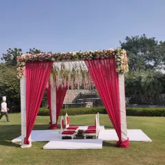 This is a classic outdoor mandap setup with a simple and elegant design. It features rich red drapes, a floral border, and traditional low seating (patlas) for the bride, groom, and priest.