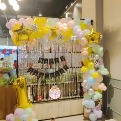 A pastel-colored balloon arch with a silver shimmer curtain, creating a fun photo backdrop for a first birthday.