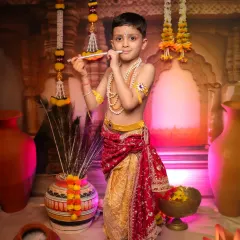 A serene portrait of a young boy as Krishna, playing his flute. Our studio setup, complete with peacock feathers and earthen pots, creates an authentic Vrindavan atmosphere for these divine photoshoots.