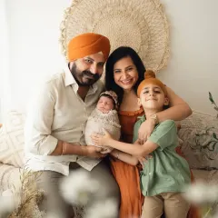 A happy family of four, including a proud big brother, posing with their new baby in my bohemian-style studio. This is a perfect family of four photoshoot idea.