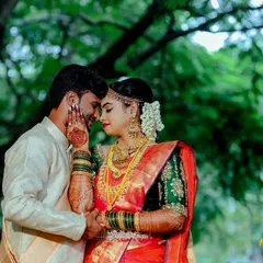 An intimate moment captured outdoors, with the groom gently holding the bride's face. Her intricate henna, traditional jewelry, and vibrant saree highlight the beauty of pre-wedding traditions.